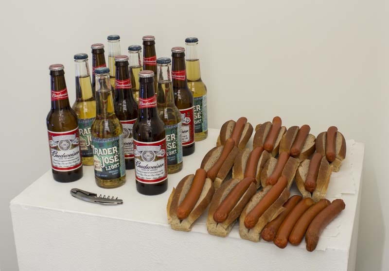 There are a stand full of different brands of beer bottles on the left, a pocket knife, and hotdogs, and a few sausages on the right. 