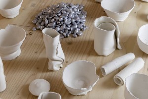 Many ceramic recipients lie glasses and bowls and a pile of silver beans placed on a wooden table