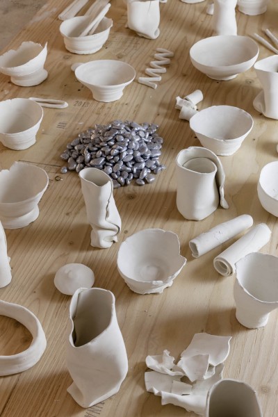 Many ceramic recipients lie glasses and bowls and a pile of silver beans placed on a wooden table 