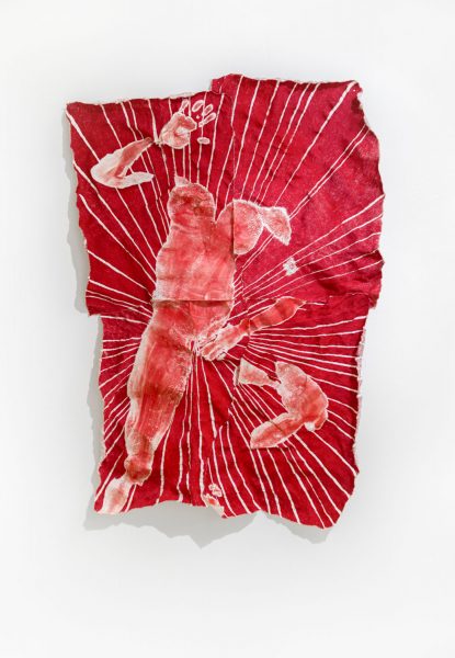 Piece of fabric dyed red with an impression of a body on it, hanging on a wall.