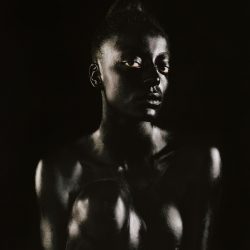 Black and white photograph of a Black woman making direct eye contact with the camera, high contrast.