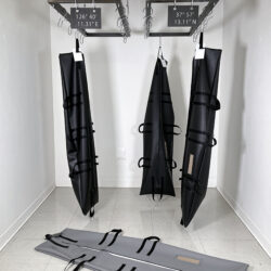 Three black body bags hanging upright with hooks attached to two separated metal racks and one grey body bag placed on the floor