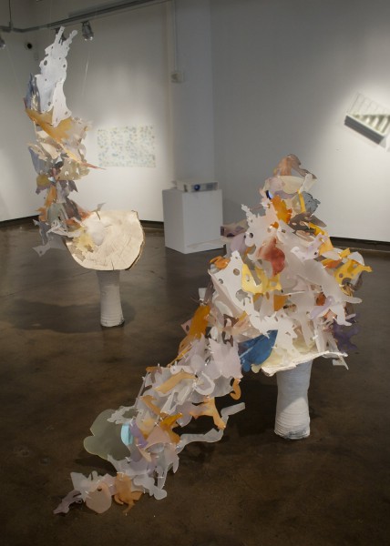 Installation view of sculpture with organic rounded and angle shapes with color inclouding frosted white, orange, blue, green, sitting on a stand.