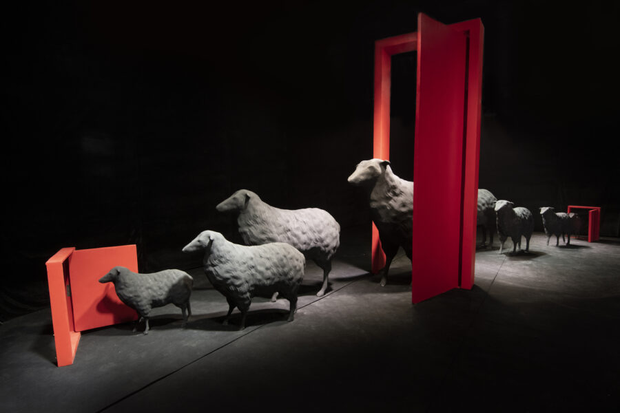 A computer rendering of a line of gray sheep going through a series of three red doors.