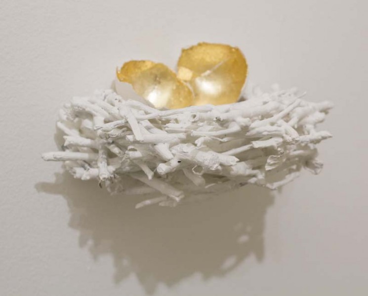 A small bird nest made of white organic materials looking like branches and two pieces of egg shell painted with gold on the inside and white on the outside