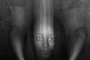 Artwork by Lewis Derogene. BFA Fine Arts, 2019. Black and white photograph of a female with her hands on a white pedestal. Head is distorted to show its transcending downward.