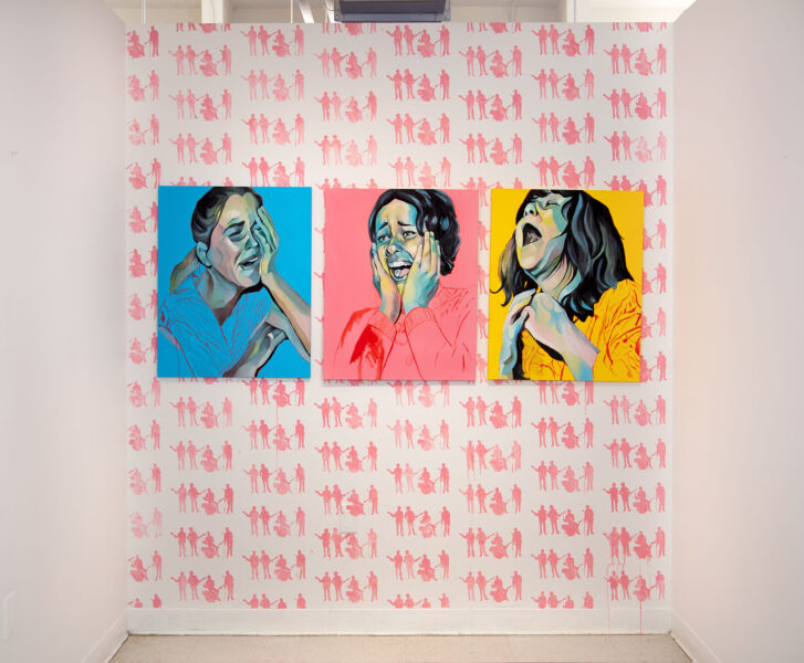 Three paintings of screaming young women are installed on the far wall of a room with 3 walls. There is a pink painting in the center, a yellow painting on the right, and a blue painting on the left. On the back wall behind the paintings there is a repeated stencil painted in pink of silhouettes of the Beatles playing their instruments.