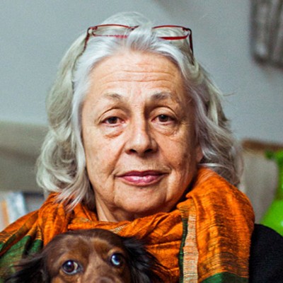 Headshot portrait of Lynda Benglis wearing an orange scarf and her dog in her lap
