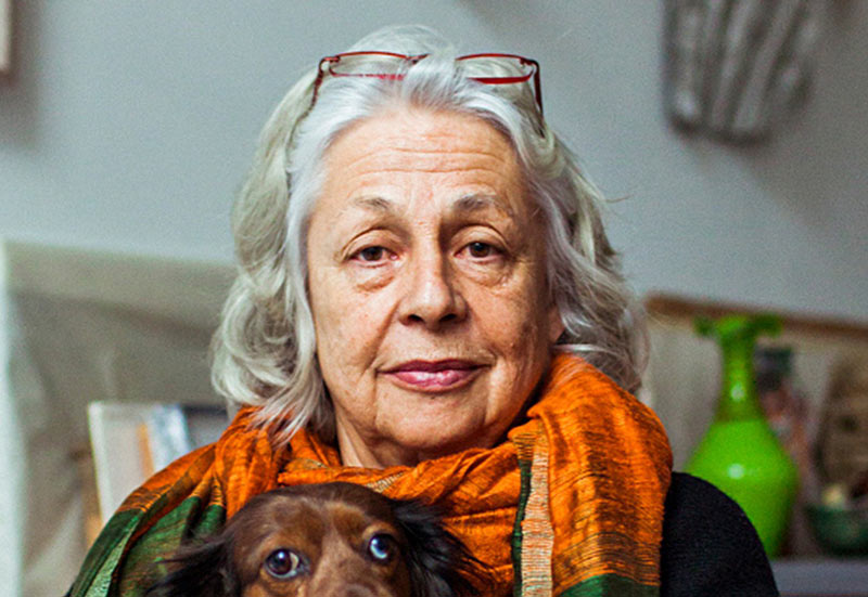 Headshot portrait of Lynda Benglis wearing an orange scarf and her dog in her lap