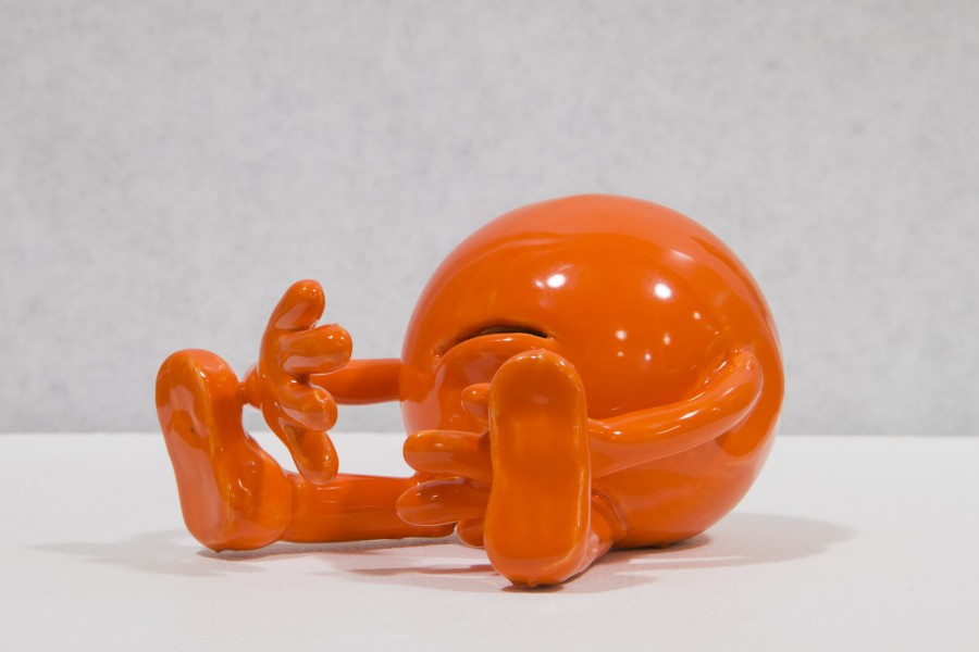 Close view of an orange sphere made of ceramic in the shape of a sphere with mouth, hands, and legs in a sitting position