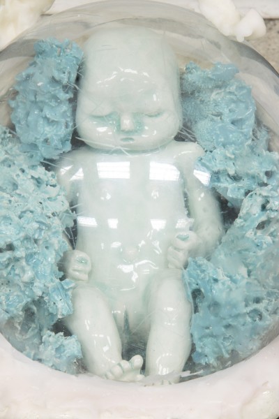 Ceramic sculpture of a tiny baby colored in light blue, sunk in liquid, surrounded by some blue organic curved materials