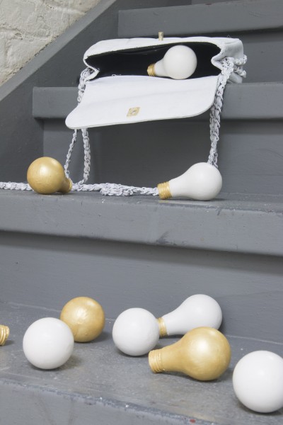 A purse on the top side of the staircase and from the purse is falling off many lightbulbs made out of ceramic. Lightbulbs are colored in white and gold.