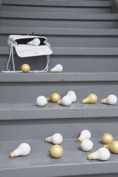 A purse on the top side of the staircase and from the purse is falling off many lightbulbs made out of ceramic. Lightbulbs are colored in white and gold.