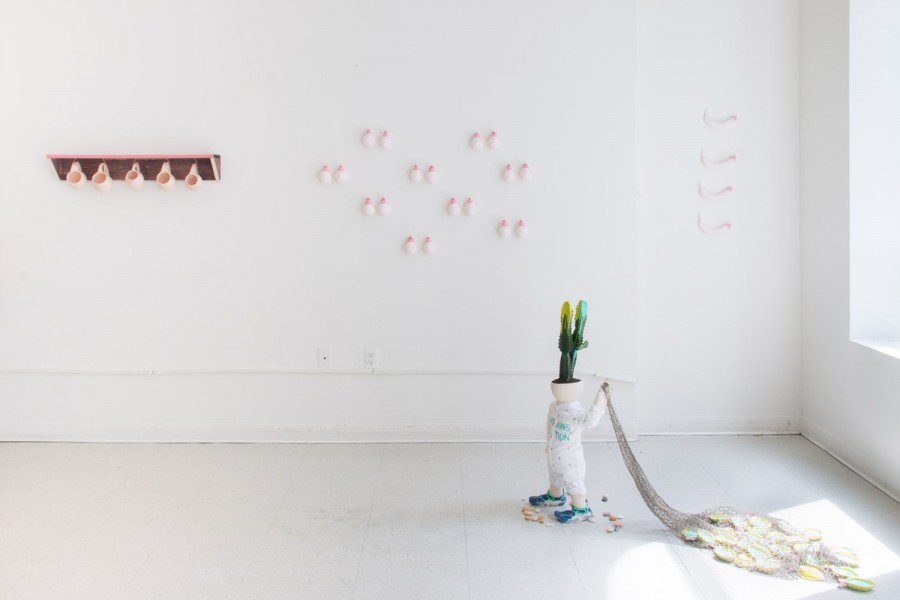 Installation view of ceramic sculptures hung on the wall and a small child-form sculpture with a cactus on the head