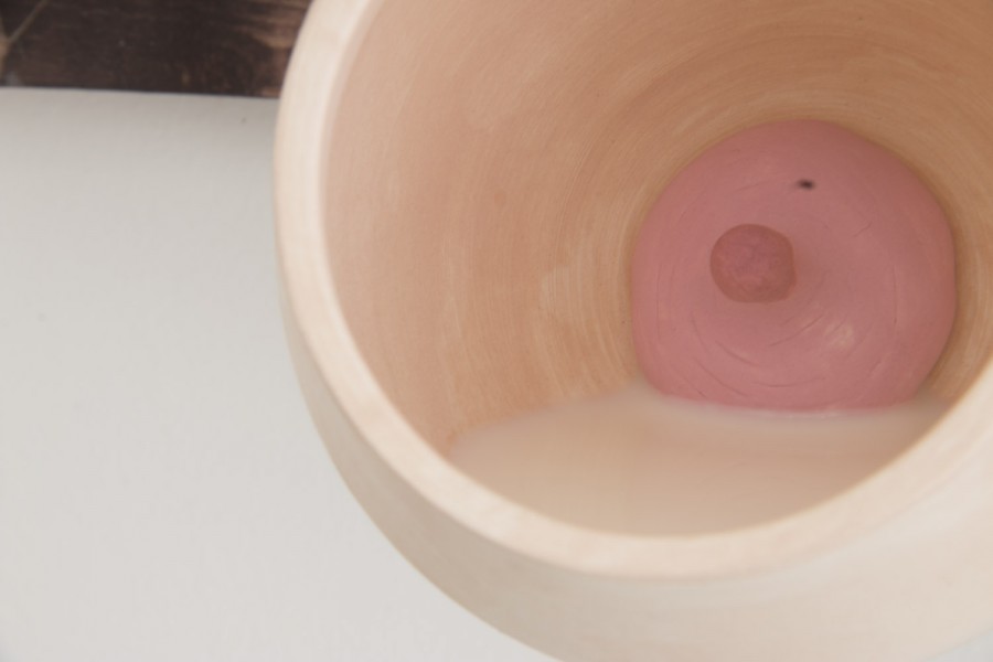 Ceramic sculpture in the shape of a rounded cup with liquid. Its color is skin-like orange. The bottom is pink with a dark orange dot in the middle m