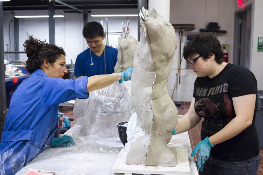 Two students working on a ceramic anthropomorphic sculpture on a table