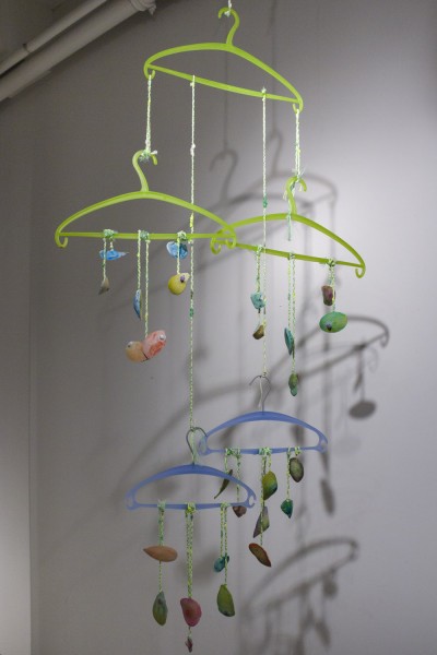 Green hangers suspended in the air with threads hanging and holding rounded organic shapes in orange, red, or blue color