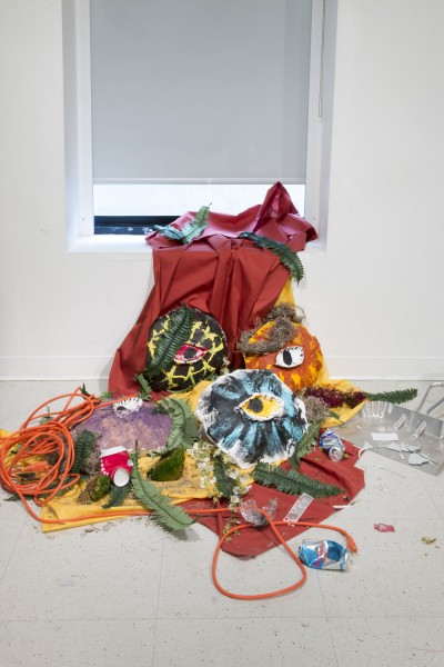 Organically shaped sculptures made from red, orange, yellow, and other color fabrics, installed near a window and on the floor