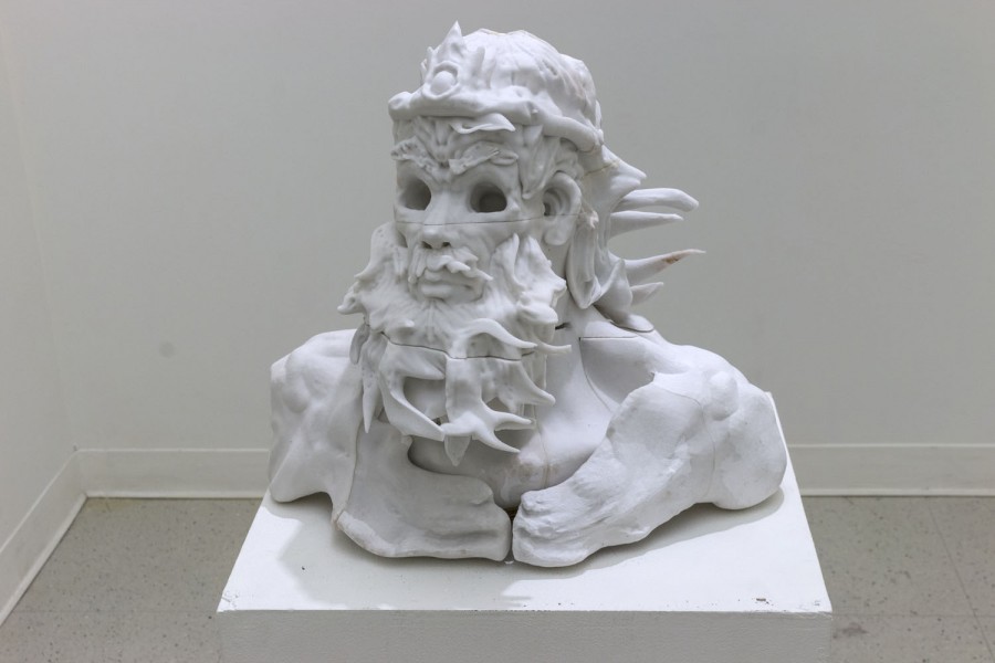 White bust sculpture of a god-like figure with long hair, long beard, and a crown, placed on a white stand