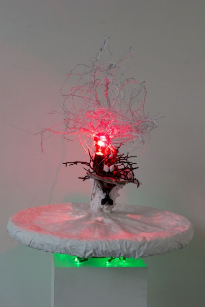 Installation of an abstract sculpture with white branches rising, and black branches at the bottom with a red light in the middle