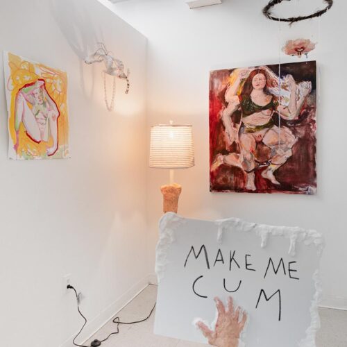 Installation view of a studio space, including a sign that says Make Me Cum and a self portrait painting.