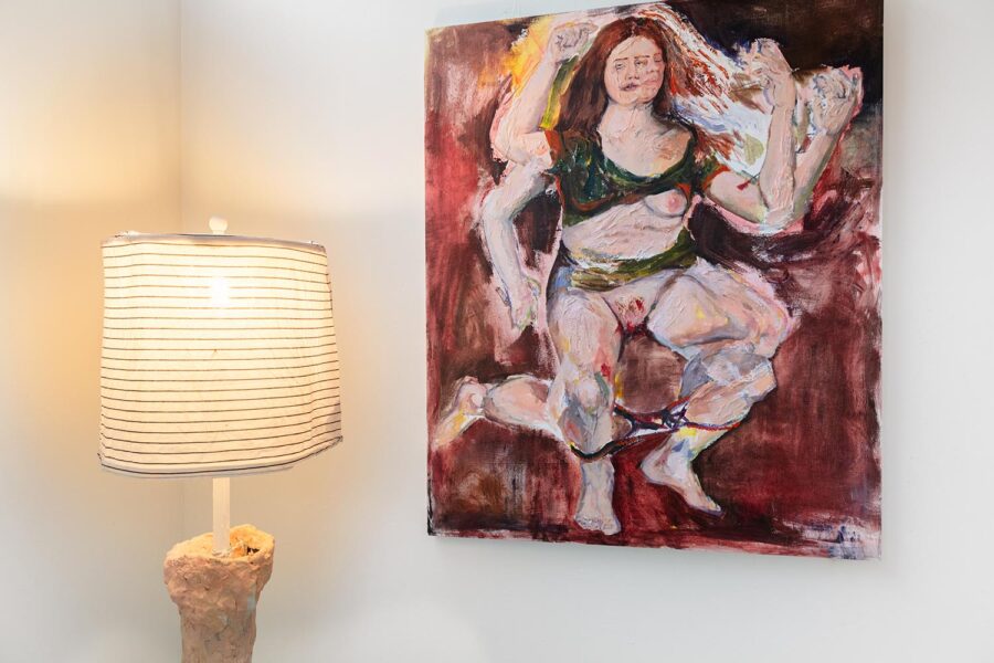 Installation view of a studio space with red a self portrait painting and a lamp in the corner.