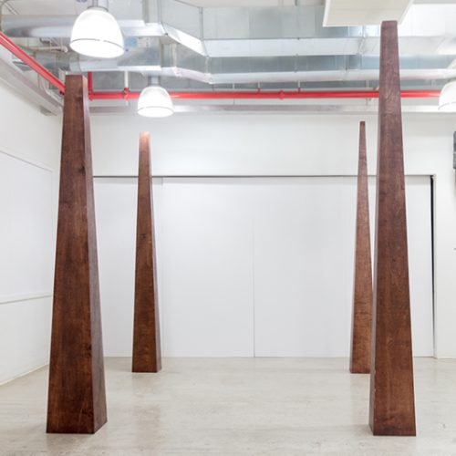 Artwork by Marc Cioffi. Four large wooden pyramid shaped sculptures.