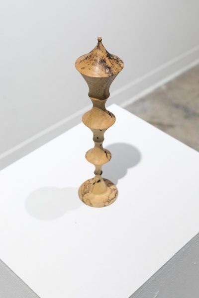 Artwork by Marc Cioffi. A sculpture of a wooden cylindrical object placed on a pedestal.