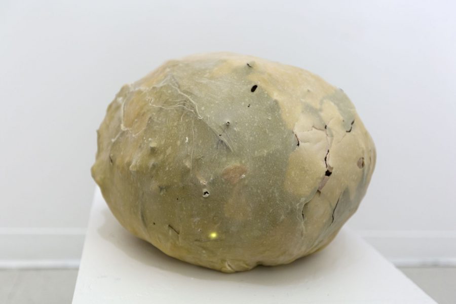 Install shot of a resin covered natural yellow/brownish orb on a white pedestal.
