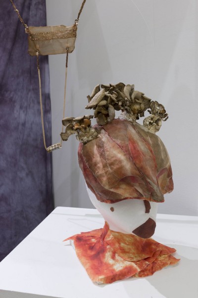 Head-shaped sculpture made of white, brown, and maroon materials and colors sitting on a table.