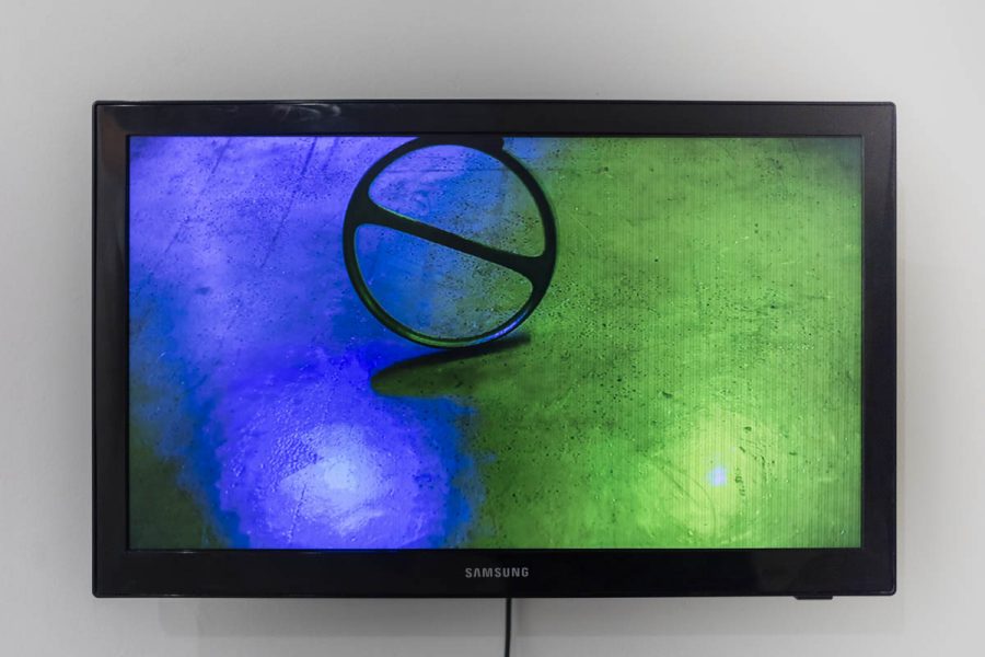 A TV displays an image with a metal wheel that has a line inside it, and the floor is illuminated with a blue light on the left and green light on the right