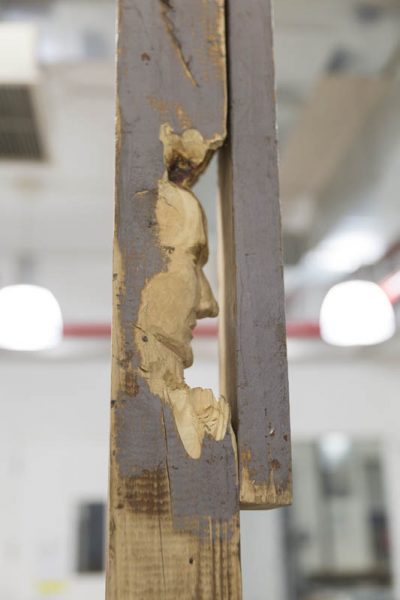 Profile of a portrait sculpture made in a used piece of wood painted in grey