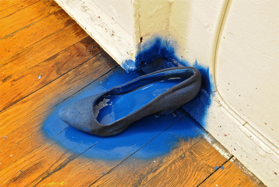 A high-heeled shoe was placed on a wooden floor and painted with blue color.