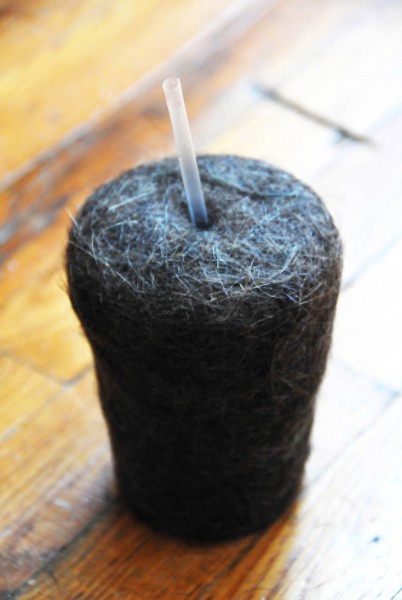 A black glass with a straw made from human hair on a wooden floor.
