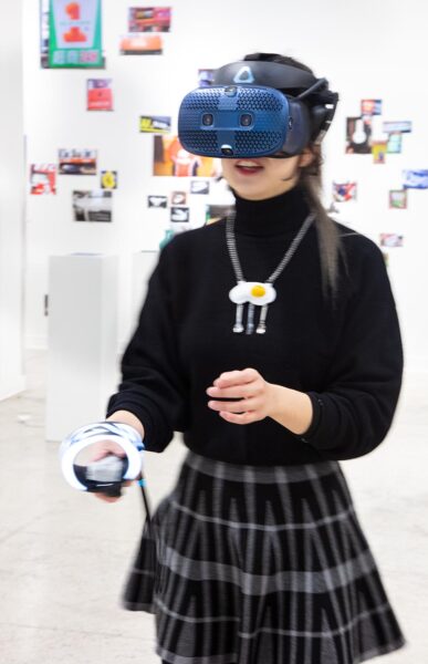 Installation view of woman wearing a VR headset in a plaid skirt.