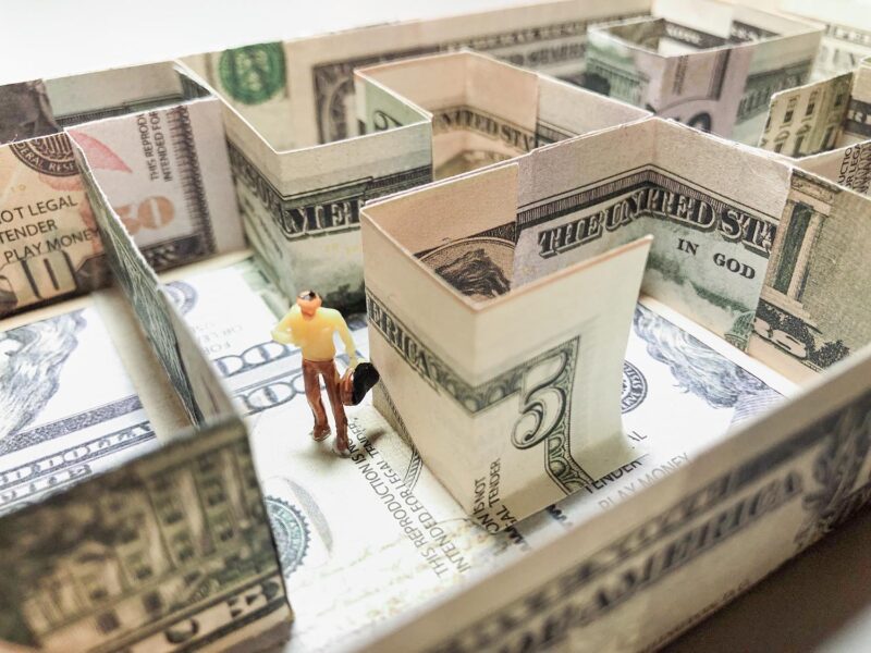 Model maze made of five dollar bills with miniature man wandering the halls.