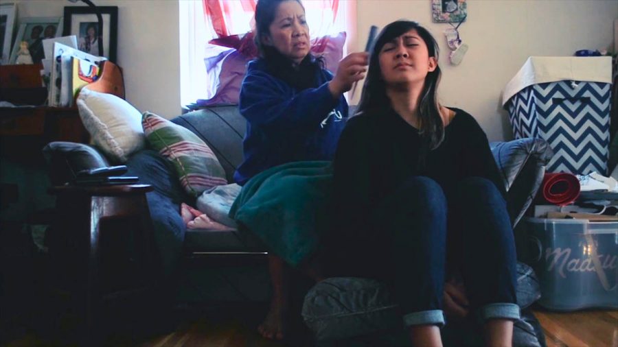 A still image from a movie with an older woman sitting on a couch and brushing the hair of a girl who is sitting on the floor in the living room