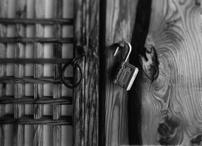 Close-up of an open lock with a cipher hanging on a wooden door lock and a metal ring on the left side of the lock.