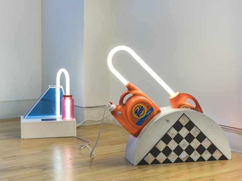 Two sculptures connected by extension cord, including neon and tide bottles.