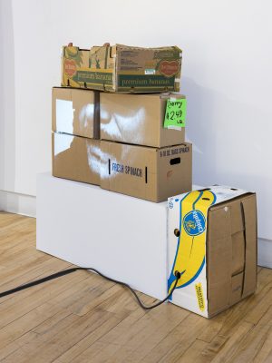 Sculpture made of stacked banana boxes with an extension cord coming out.