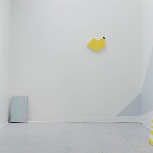 Installation view of different shaped media with blue, light blue, yellow and white and yellow stripes hanging on the wall and near the wall.