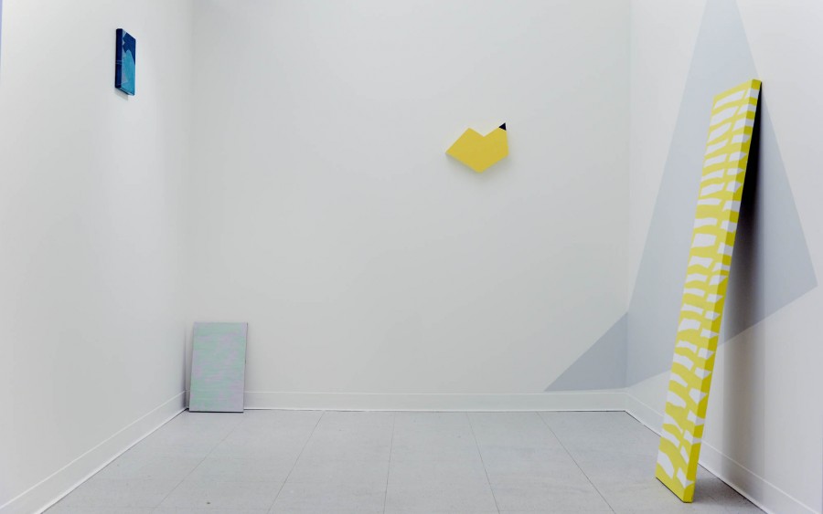 Installation view of different shaped media with blue, light blue, yellow and white and yellow stripes hanging on the wall and near the wall.