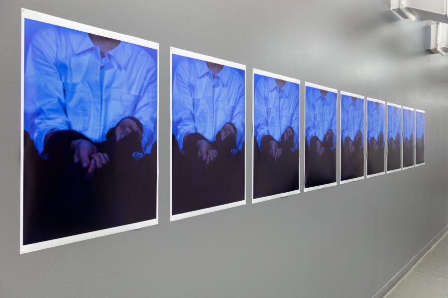 Install shots of nine prints on a wall of a man with a rope around his wrists wearing a blue shirt.