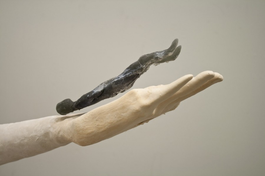 Sculpture of a hand with the palm open and a small black anthropomorphic sculpture in the palm