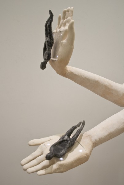 Sculpture of two hands with the palms open and them are holding small black anthropomorphic sculptures