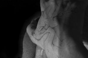 Black and white photograph of a naked torso with hands covering male genitalia and a black and white image projected on top of the person of more male genitalia.