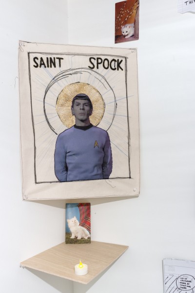 Composite work made of a cut-out of Spock from Star Wars with a saint aura and SAINT SPOCK written at the top, two small prints of a kitten, and a led candle light on a shelf.
