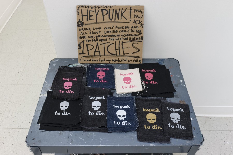 Too punk to dye with a skull message print on many pieces of dark fabrics and cardboard with the message: HEY PUNK! Yea, you! Wanna look cool? Punkers are all about looking cool! Do you hate cops, the government + capitalism?! Too bad about the last one. Give me $. $1 patches. If I'm not here, feed my numb skull yes dollars.