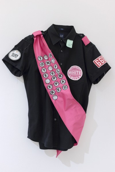 Black shirt with white, red and pink patches on it and a pink diagonal belt with the message I don't feel prepared written in small white circles for each letter and blank space