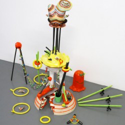 Installation view of a sculpture made of different colored pieces in green, yellow, ceramic objects installed on top of each other, on the floor